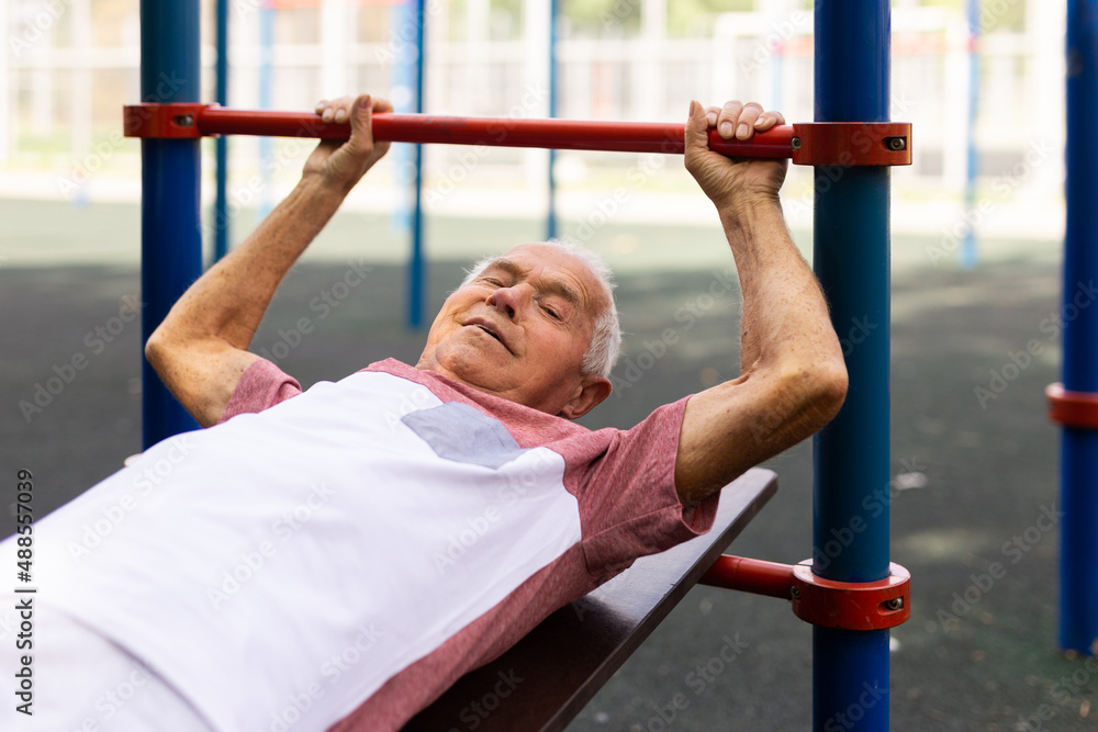 Fototapeta premium Open air gym. Street training on the municipal sports equipment. Elderly man pumps the press in city park