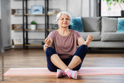 sport, fitness and healthy lifestyle concept - happy senior woman meditating on exercise mat at home