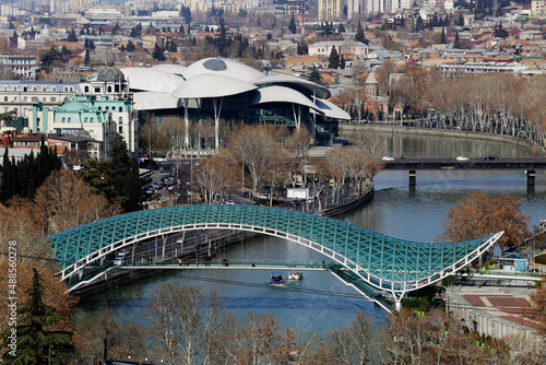 Aerial view of the Bridge of Peace, a pedestrian bridge made of steel and glass with a curvy design, over the Kura Mtkvari river in Tbilisi, Georgia. The Public Service Hall is seen in the background.