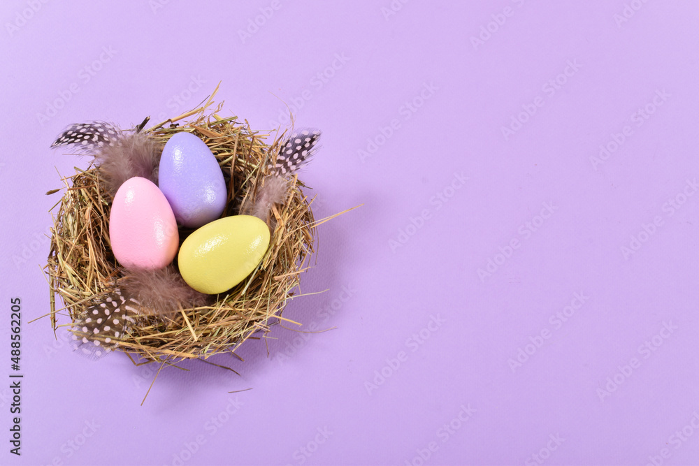 Three painted eggs lie in a nest on a purple background. The minimum composition of Easter. Three painted eggs lie in a nest on a purple background. The minimum composition of Easter.