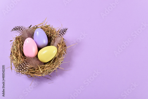 Three painted eggs lie in a nest on a purple background. The minimum composition of Easter.