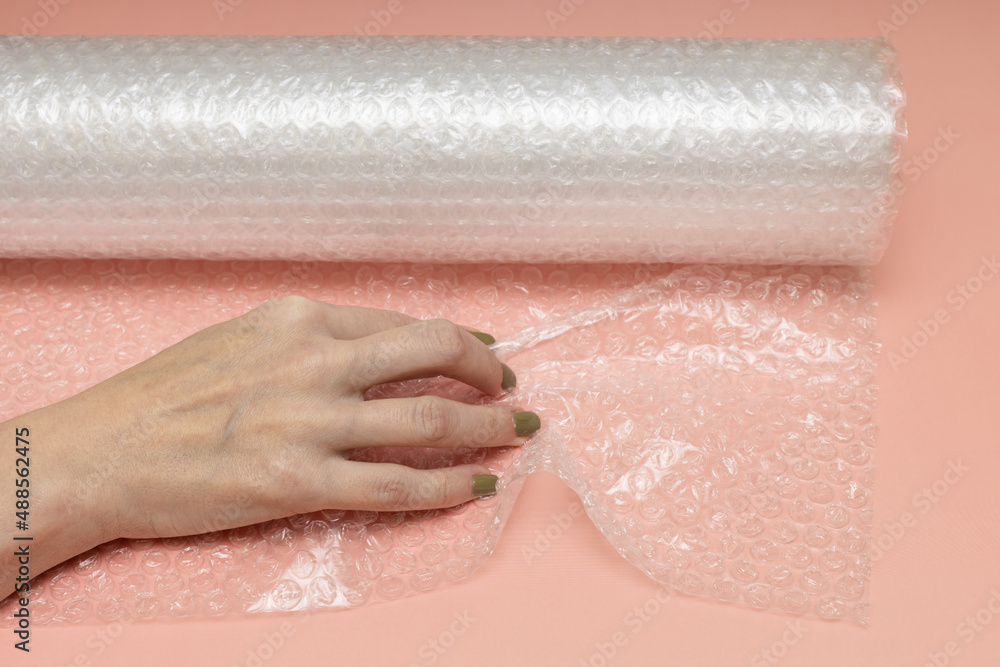 Fototapeta premium female hand crumples bubble wrap on a pink background