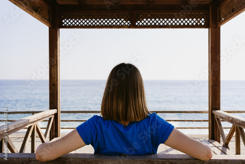 Woman in a blue t shirt enjoy the view of the sea while sitting on a wood bench © diignat