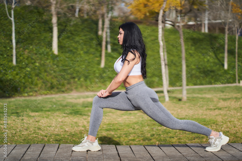 young woman in sportswear and sneakers doing squats while working out in the park on a sunny day young woman in sportswear and sneakers doing squats while working out in the park on a sunny day