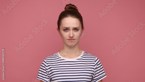 Serious attractive woman with hair bun nodding no, expressing disagreement, looking at camera with rejection, wearing striped T-shirt. Indoor studio shot isolated on pink background. photo