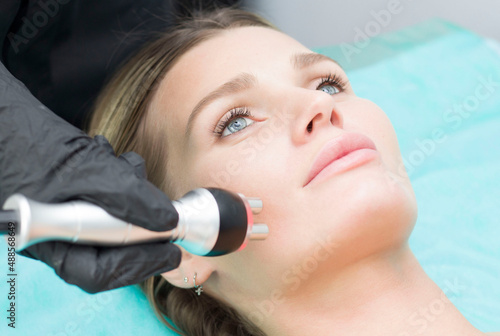 A young woman is lying on the RF-lifting procedure for face skin tightening and face contour correction. Close-up.