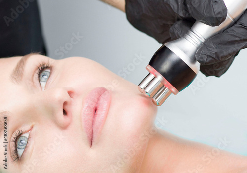 A young woman is lying on the RF-lifting procedure for face skin tightening and face contour correction. Close-up. photo