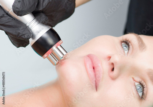 A young woman is lying on the RF-lifting procedure for face skin tightening and face contour correction. Close-up.