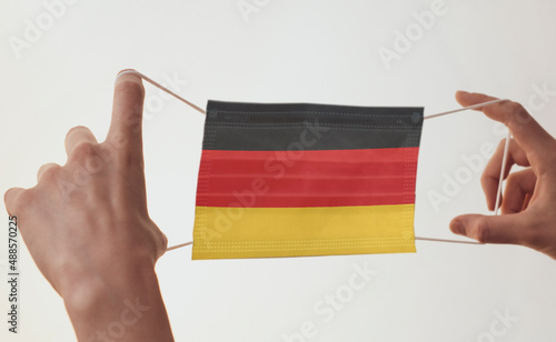 Female hands hold a medical mask with the flag of Germany. National flag and protective mask on a light background.