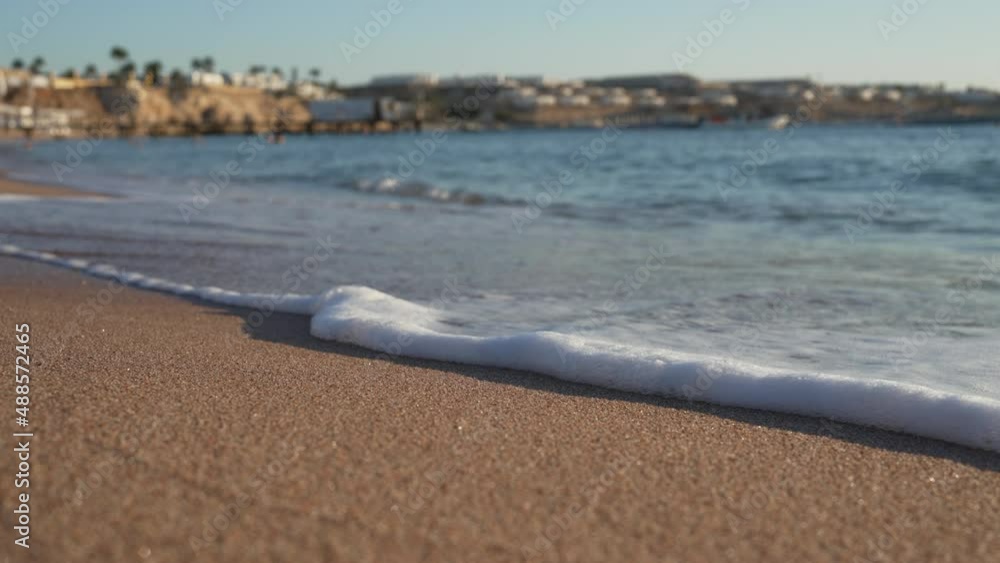Sea waves on sandy beach, white houses and palm trees on blurred background. Summer holidays in beautiful lagoon, natural background Sea waves on sandy beach, white houses and palm trees on blurred background. Summer holidays in beautiful lagoon, natural background