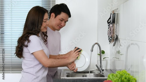 happy young couple washing dishes together in the sink in the kitchen at home. 4k Video.