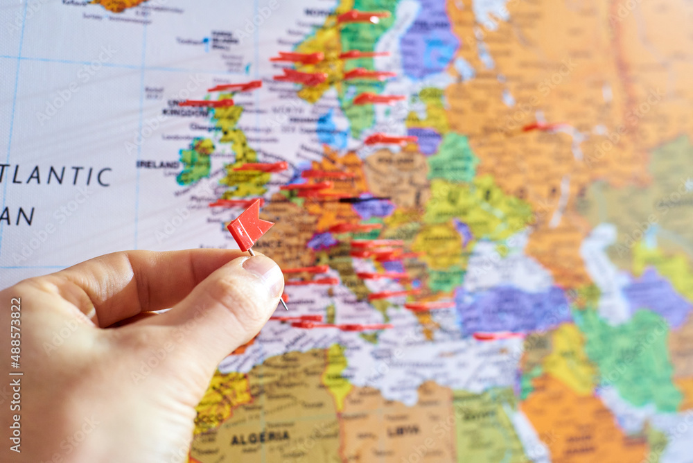 Eine Hand setzt gerade eine Pin Markierung auf eine Landkarte, Ausschnitt liegt auf Europa - Reise, Weltreise - obrazy, fototapety, plakaty 