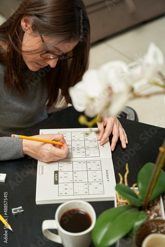 Woman playing sudoku game at home in a game book , alone