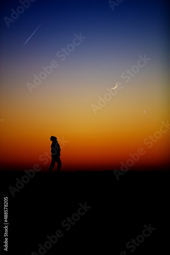 Man observing evening sky with stars, planets, falling stars and crescent Moon.