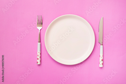 white empty plate and knife with a fork on a pink background