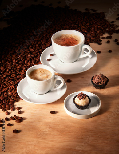 Xícaras com café expresso e Cappuccino, em fundo de madeira com doces e grãos de café torrados 