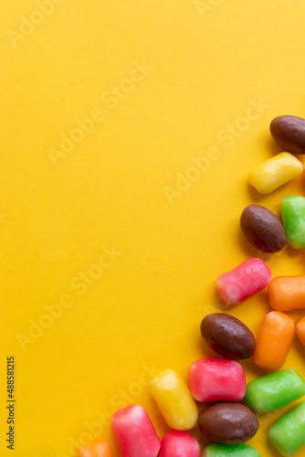 Bright yellow background with colored sweets and chocolate eggs for children. Easter background with copy space photo