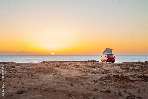 gemütliches Van Life mit Camper an Küste im Sommer bei Sonnenaufgang /  Sonnenuntergang im Gegenlicht der Sonne