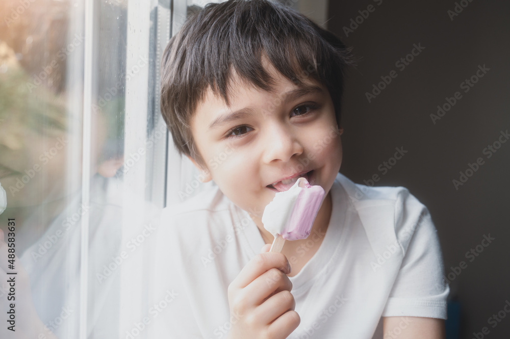 A Happy kid eating some ice cream, Portrait of a handsome young boy sitting next to a window having a refreshment, Child with a smiling face relaxing at home. Kid looking at camera A Happy kid eating some ice cream, Portrait of a handsome young boy sitting next to a window having a refreshment, Child with a smiling face relaxing at home. Kid looking at camera