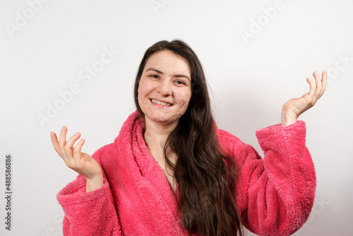 A young brunette woman in a pink bathrobe makes cleansing facial treatments - a mask or scrub to cleanse and nourish the skin.