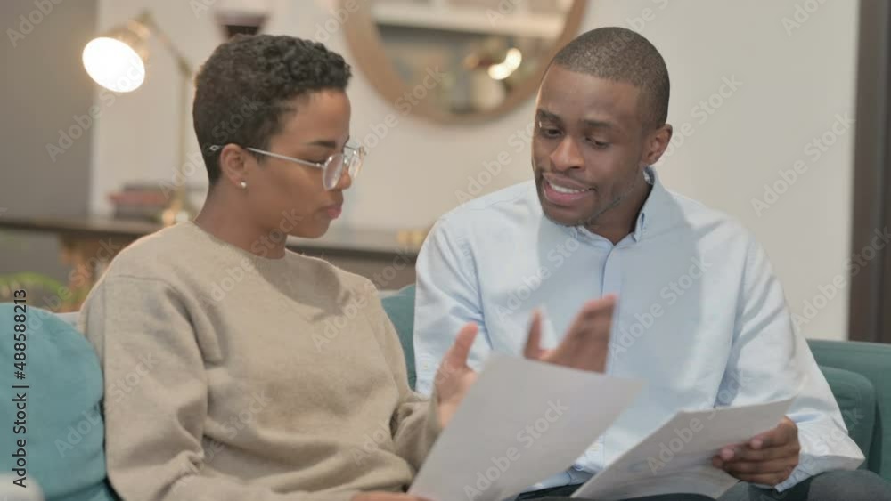 Couple Arguing while Reading Documents on Sofa Couple Arguing while Reading Documents on Sofa