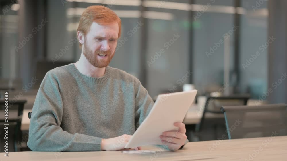 Young Man Upset while Reading Documents in Office Young Man Upset while Reading Documents in Office