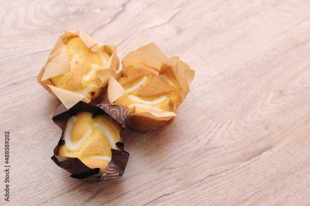 Cupcakes in brown paper cups are placed on a light wooden table. Cupcakes in brown paper cups are placed on a light wooden table.