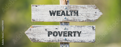 Photos opposite signs on wooden signpost with the text quote wealth poverty engraved