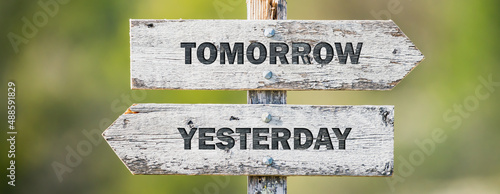opposite signs on wooden signpost with the text quote tomorrow yesterday engraved. Web banner format. photo