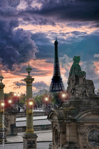 Espectacular e inusual vista de la Torre Eiffel en Paris al atardecer desde el Campo de Marte entre columnas doradas y bajo un cielo imponente de distintos tonos.