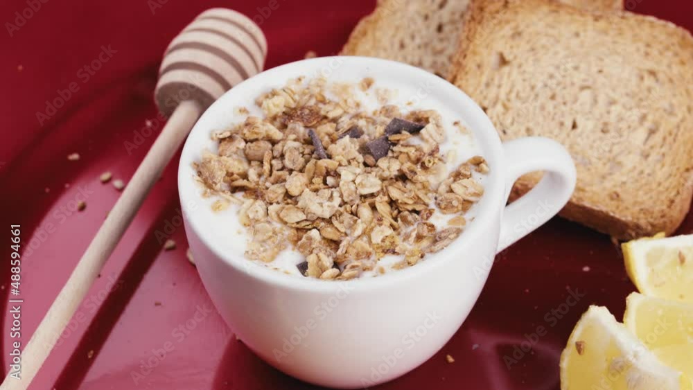 Cup of white Greek yogurt with crunchy granola in a rotating red plate Cup of white Greek yogurt with crunchy granola in a rotating red plate
