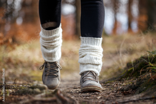 Woman walking on footpath in forest. Kintted leg warmers on hiking boot