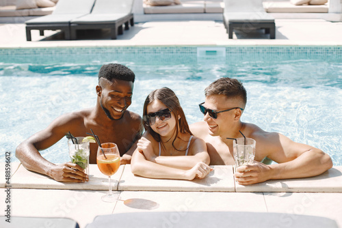 Three friends in a swimwears relaxing with a cocktails near swimming pool
