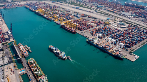 container ship and tugboat sailing in sea and commercial port working crane bridge loading container for import export, shipping or transportation concept background..