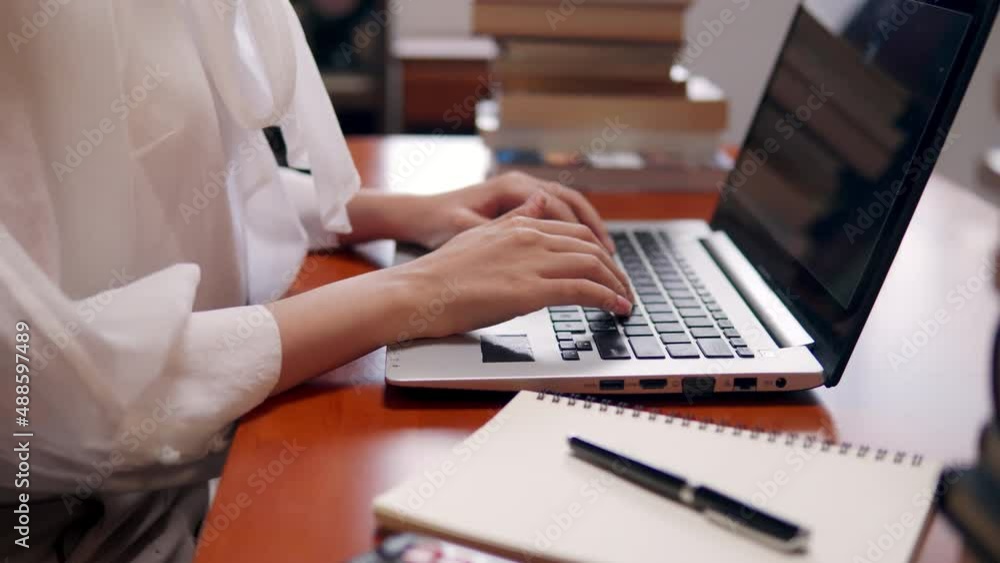 Normal angle shot of beautiful happy Asian woman sitting in front her computer laptop typing and working online over living room bookshelf as background. Normal angle shot of beautiful happy Asian woman sitting in front her computer laptop typing and working online over living room bookshelf as background.