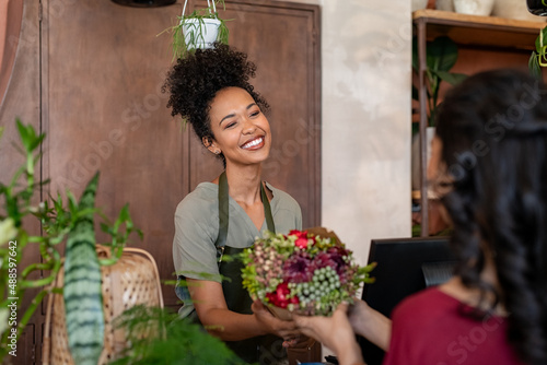Happy black florist selling flowers to young woman photo