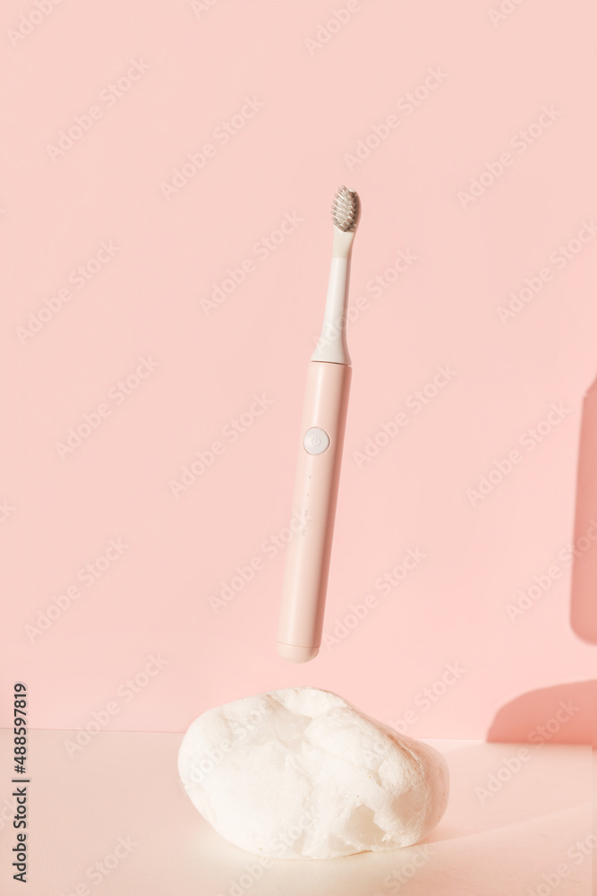 Flying modern ultrasonic toothbrush. Dental care supplies on white stone on pink pastel background. Oral hygiene, dental and gum health, healthy teeth. Dental products Wireless control. Flying modern ultrasonic toothbrush. Dental care supplies on white stone on pink pastel background. Oral hygiene, dental and gum health, healthy teeth. Dental products Wireless control.