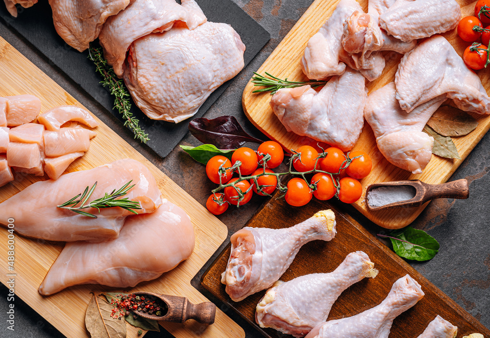 Prepared for frying, butchered various portions of raw chicken meat. Set of raw chicken fillet, thigh, wings, strips and legs on the background of the culinary table with spices and cherry tomatoes