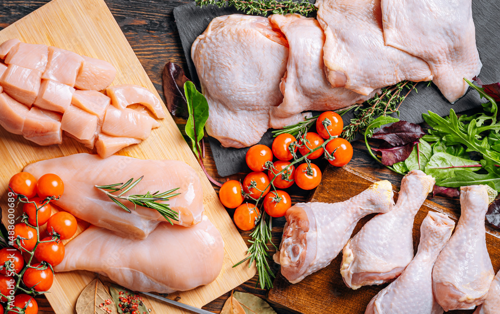 Prepared for frying, butchered various portions of raw chicken meat. Set of raw chicken fillet, thigh, wings, strips and legs on the background of the culinary table with spices and cherry tomatoes