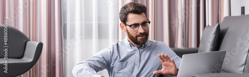 cheerful man in eyeglasses gesturing and talking during video call on laptop, banner