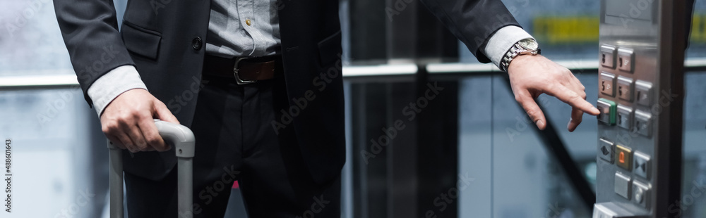 Naklejka premium cropped view of man with baggage pressing button in modern elevator, banner