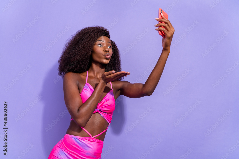 Photo of sweet flirty african lady dressed pink sexy clothes sending kiss recording video modern device isolated violet color background Photo of sweet flirty african lady dressed pink sexy clothes sending kiss recording video modern device isolated violet color background