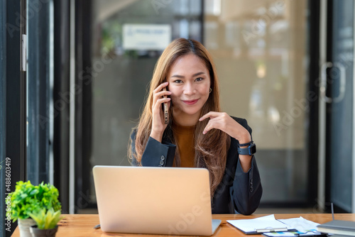 Beautiful smiling young Asian businesswoman at work talking on phone.