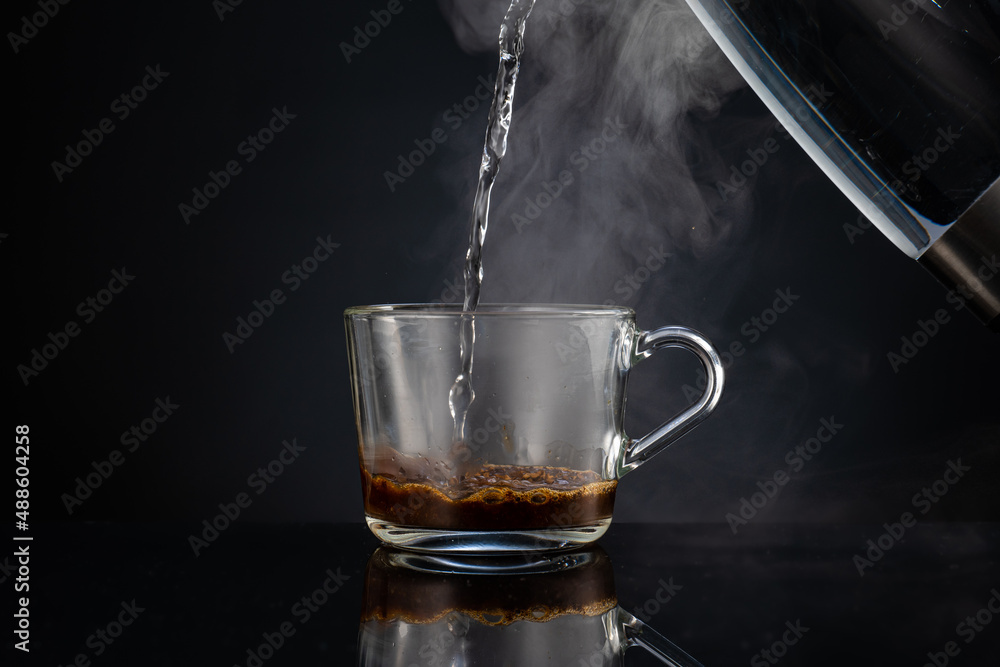 pouring boiling water into coffee in a transparent glass empty mug on a dark background pouring boiling water into coffee in a transparent glass empty mug on a dark background