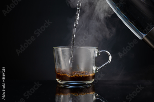 pouring boiling water into coffee in a transparent glass empty mug on a dark background