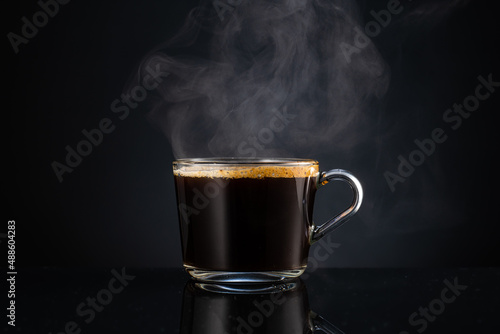 hot steaming fragrant coffee with steam, smoke in a transparent glass cup on a dark background