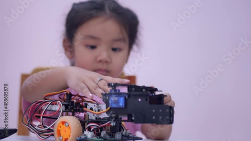 Slow motion scene of Asian girls in glasses holding a robot. A girls in a pink shirt and glasses sits at a table in front of him having a robot made by a girls. He is very satisfied with his work.
