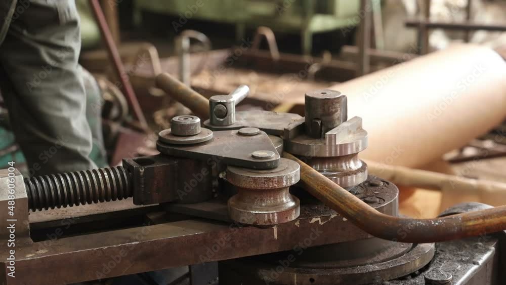 a worker works on a pipe bending machine bends pipes and takes out the finished metal billet a worker works on a pipe bending machine bends pipes and takes out the finished metal billet
