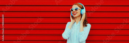 Portrait of happy smiling young woman listening to music in headphones on colorful red background