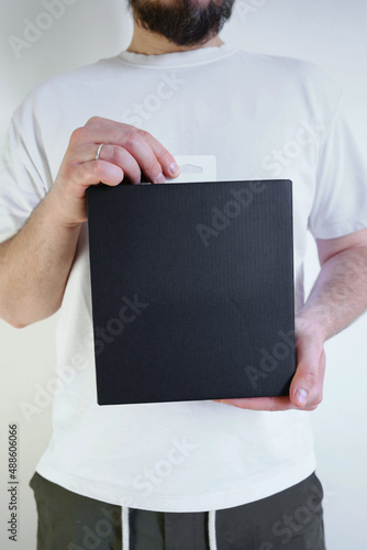 Man holds a black paper box in his hand. Young man with new package. Postal services, delivery. Kraft paper. Gift box, gift. Box close-up. Empty packaging, empty space. Cardboard case
